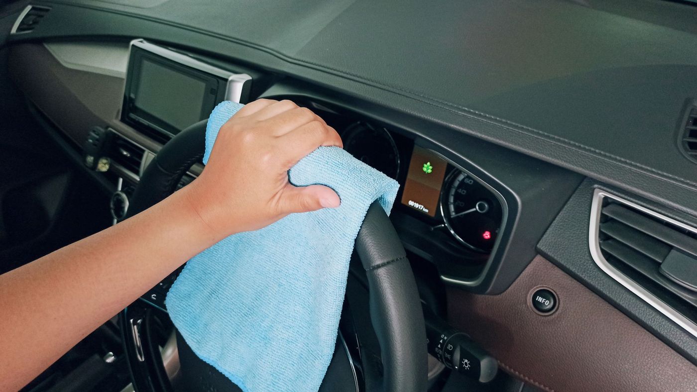 A detailer wiping down a car dashboard and steering wheel with a microfibre cloth