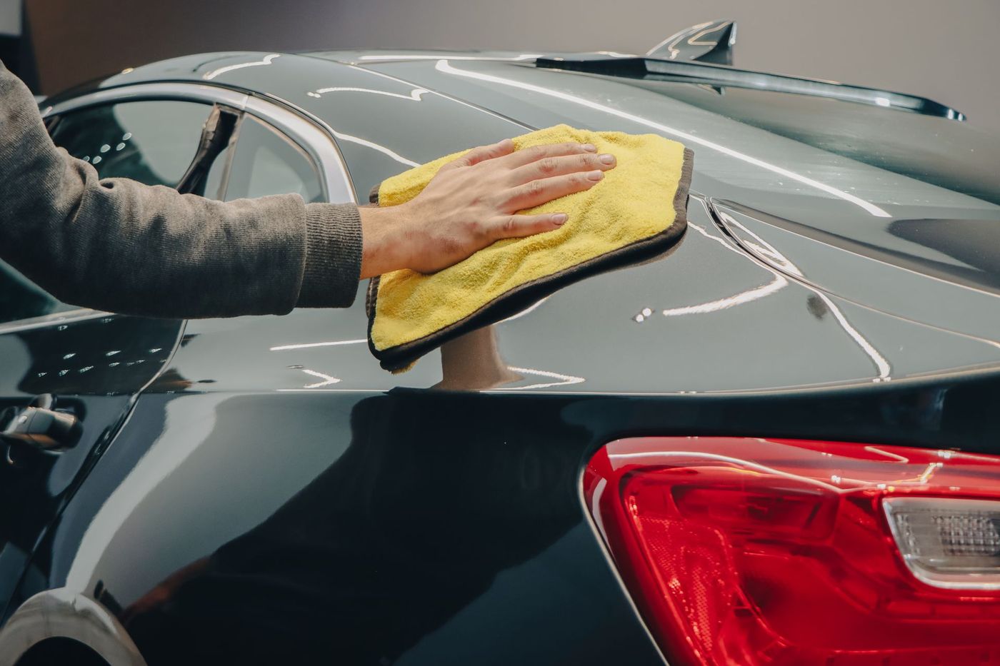 A detailer wiping down a car bonnet with a blue microfibre towel